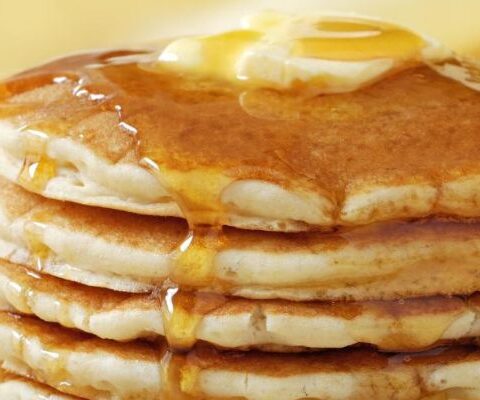 Imagem de panquecas americanas douradas, cobertas com mel e manteiga, representando a perfeição do café da manhã.